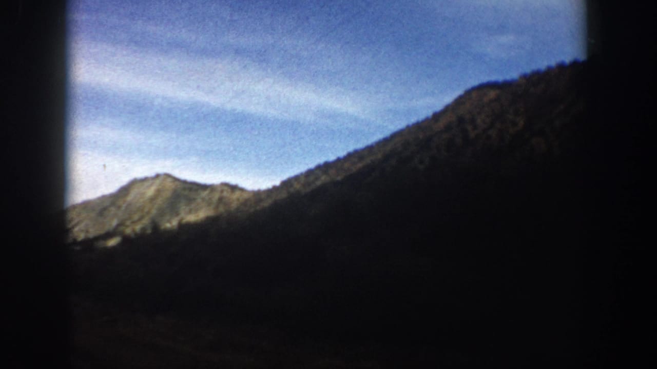 Mountain peak and dark valley slope beneath a blue sky, framed by black edges.
