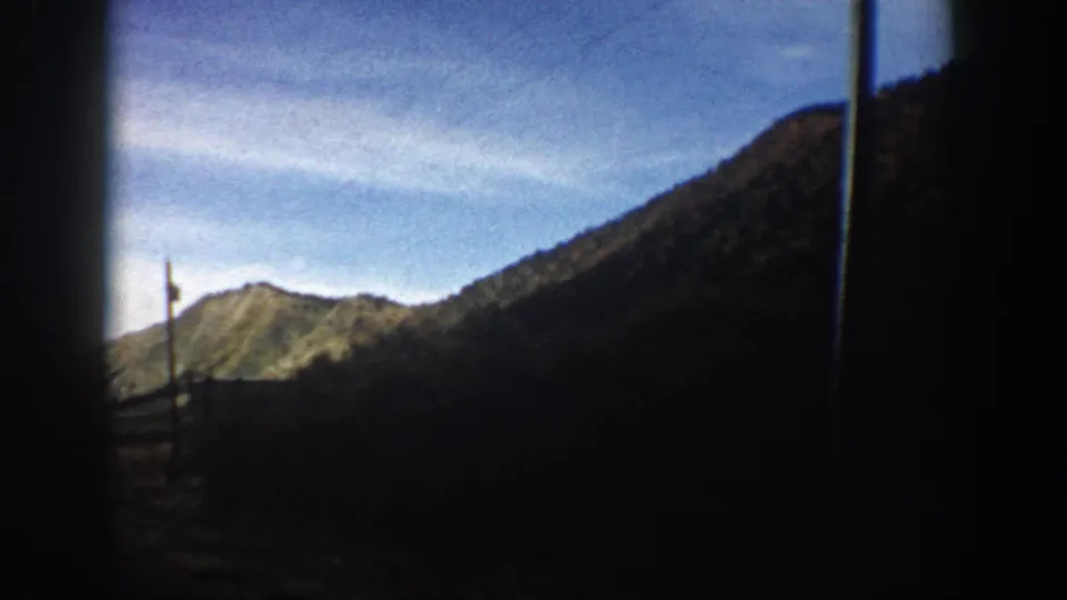 Aspen-area 1961 8mm frame showing a mountain valley and utility pole in the foreground beneath a bright blue sky.