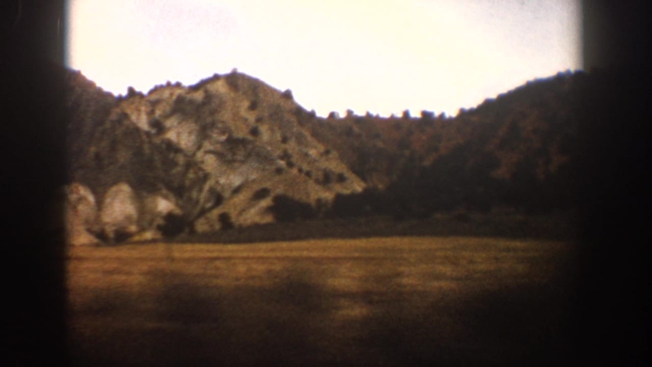 1961 Aspen-area train-window view of a rocky hillside, sparse trees, open ground, and pale sky on 8mm film.