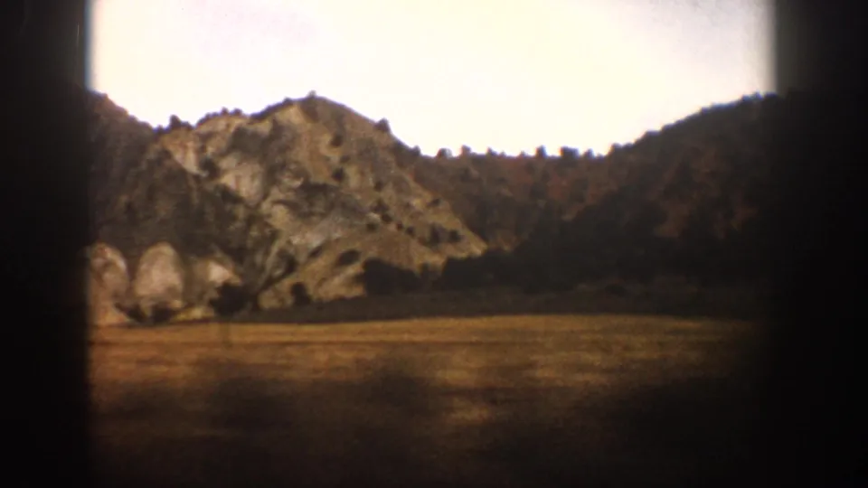 1961 Aspen-area train-window view of a rocky hillside, sparse trees, open ground, and pale sky on 8mm film.