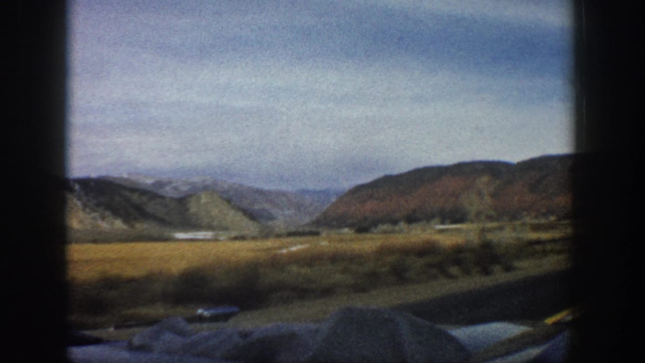 Open mountain valley with distant ridges, roadside edge, and car interior shadows.