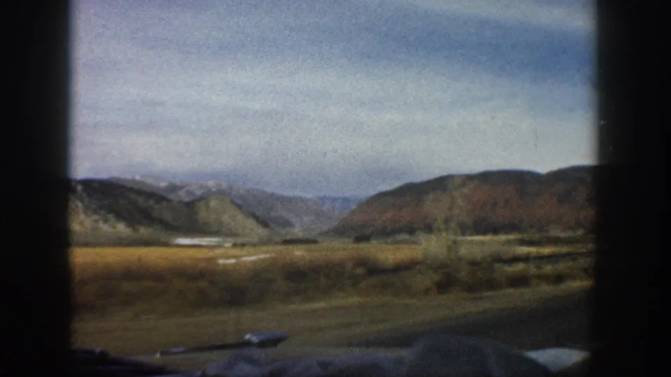 Aspen, Colorado road-view frame from 1961 showing wide valley grassland, hills, and cloudy sky on 8mm film.