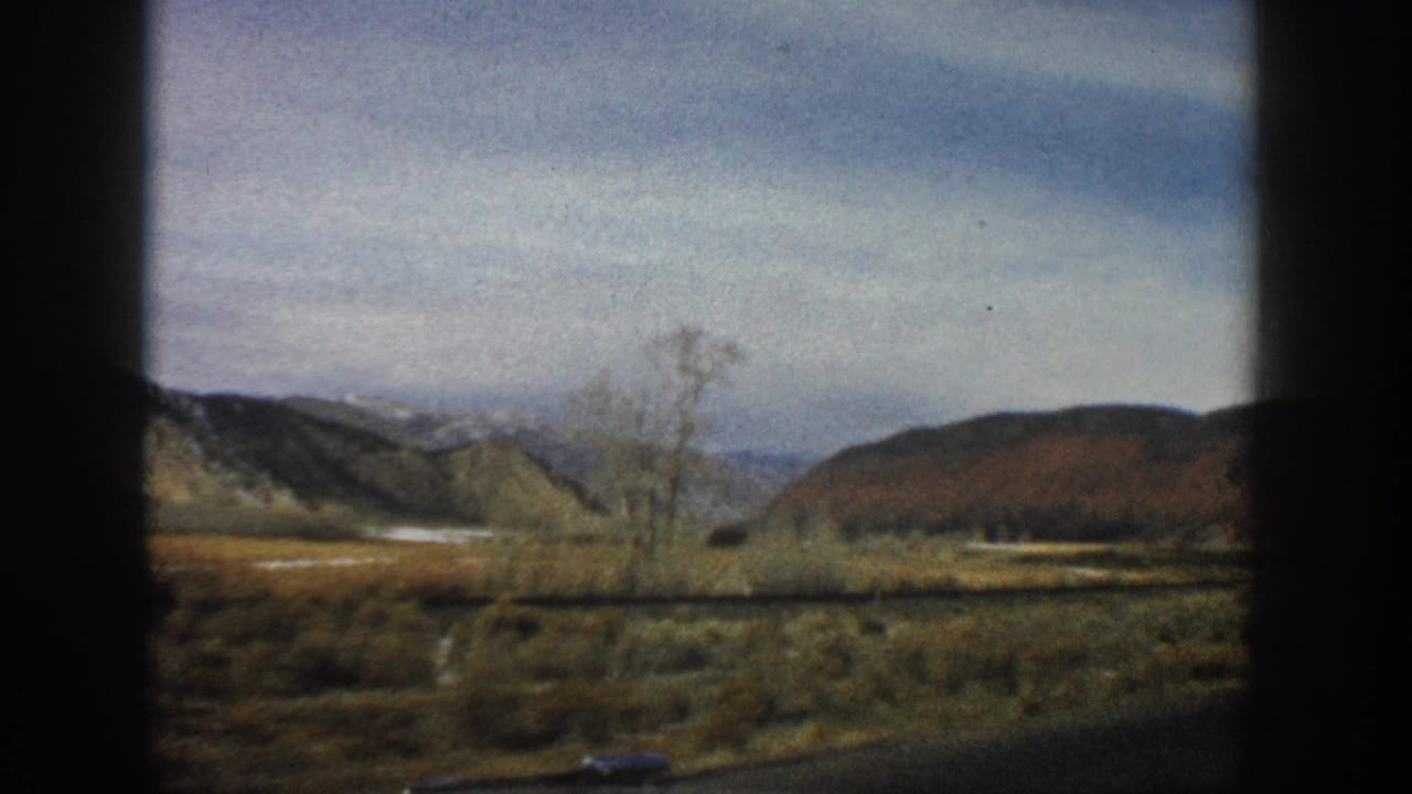 1961 Aspen, Colorado home-movie view of low hills, shrubs, and a bare tree framed by a vehicle window.