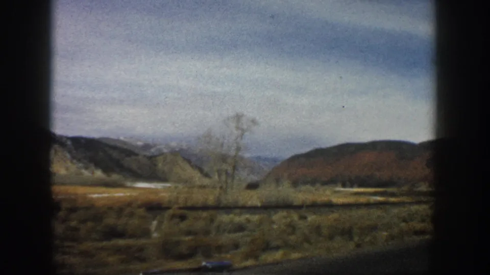 1961 Aspen, Colorado home-movie view of low hills, shrubs, and a bare tree framed by a vehicle window.