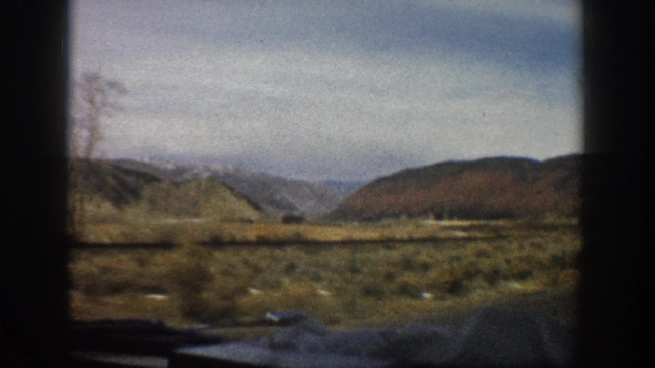 Open mountain landscape with shrubs and distant slopes seen through car-window framing.