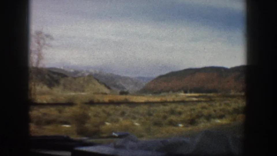 Passenger-side 8mm view near Aspen, Colorado, showing scrubby terrain and rounded hills under a pale sky.