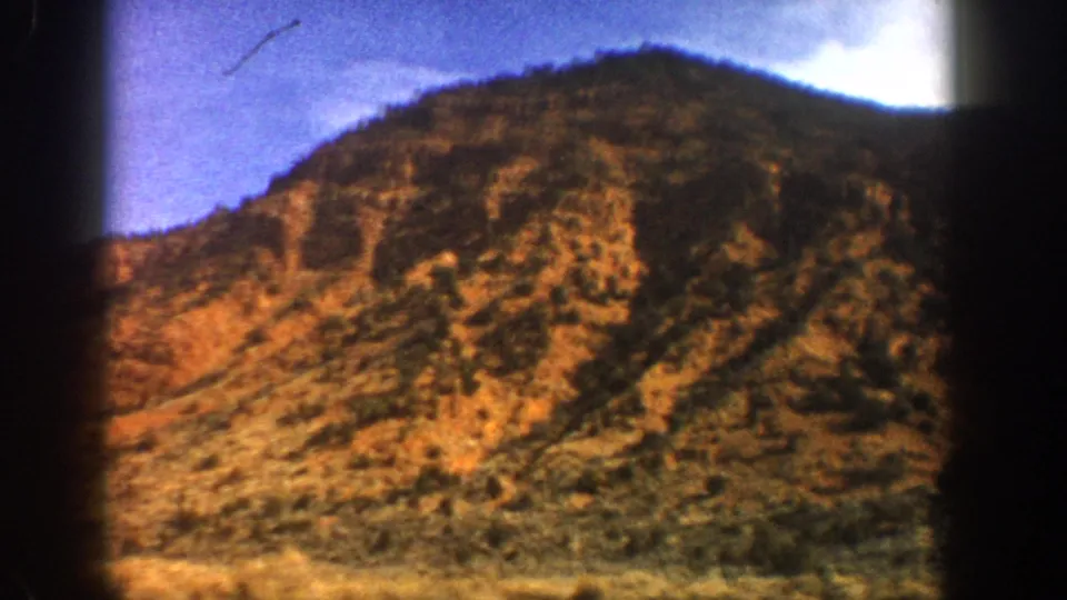 Soft 8mm frame from Aspen, Colorado, showing a rugged shrub-covered hillside as the car continues past.