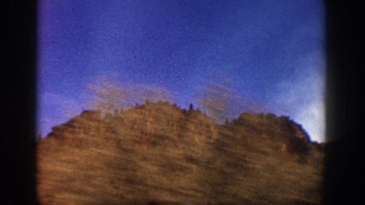 Aspen, Colorado home-movie frame from 1961 showing a brown mountain hillside under blue sky, with dark film-frame borders visible.