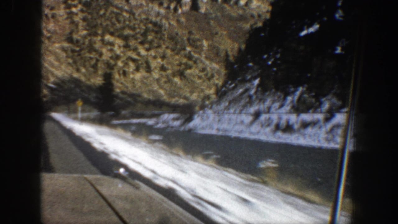 Snow-lined mountain highway beside rocky slopes, viewed from a moving vehicle.