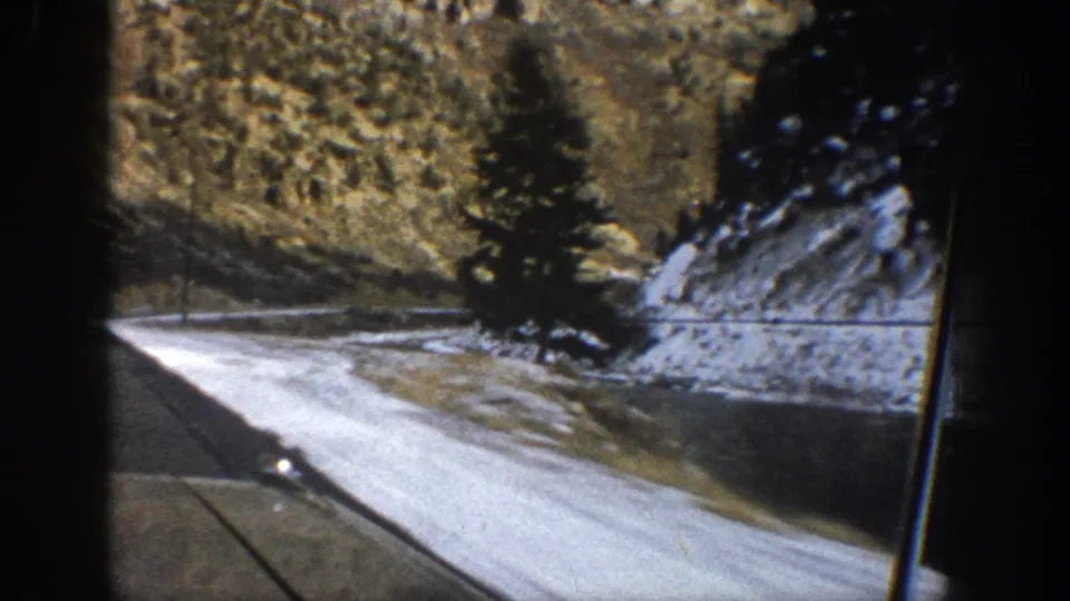 1961 Aspen-area mountain road filmed from inside a moving car, with snow along the roadside and a windshield wiper in view.