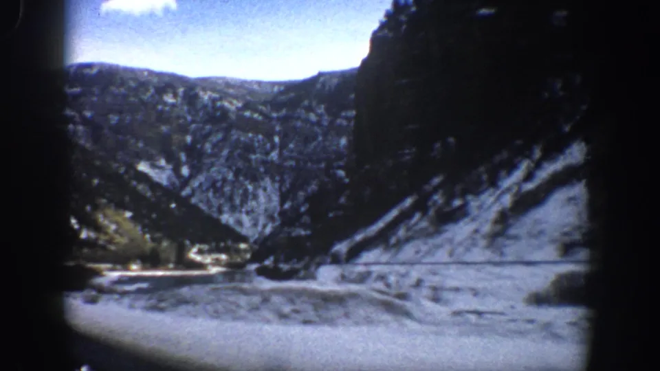 1961 home-movie frame from near Aspen showing a snowy river bend and forested mountain slopes.
