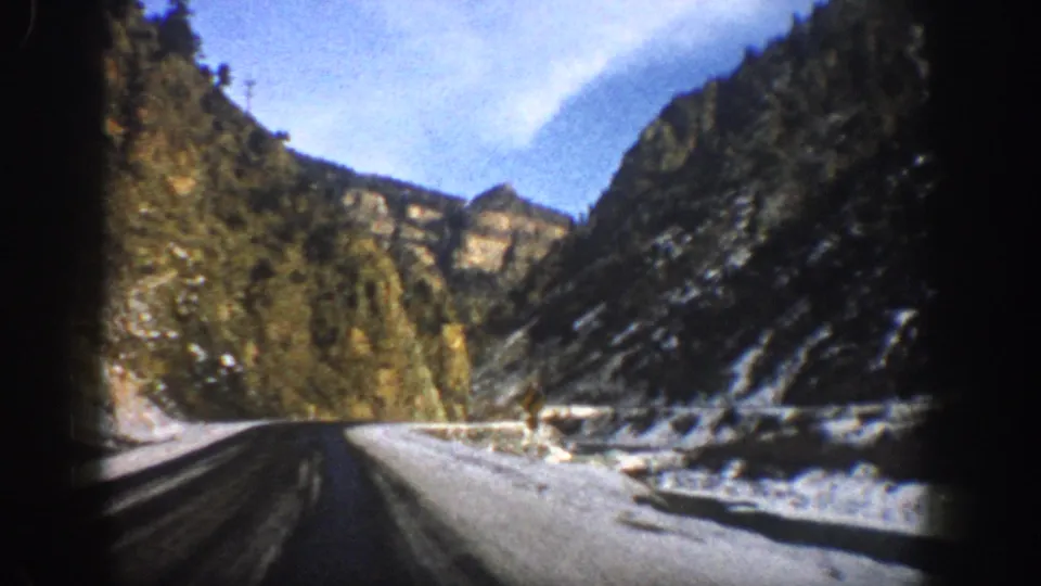 1961 Aspen, Colorado 8mm frame showing a two-lane road through a snowy mountain canyon under a bright blue sky.
