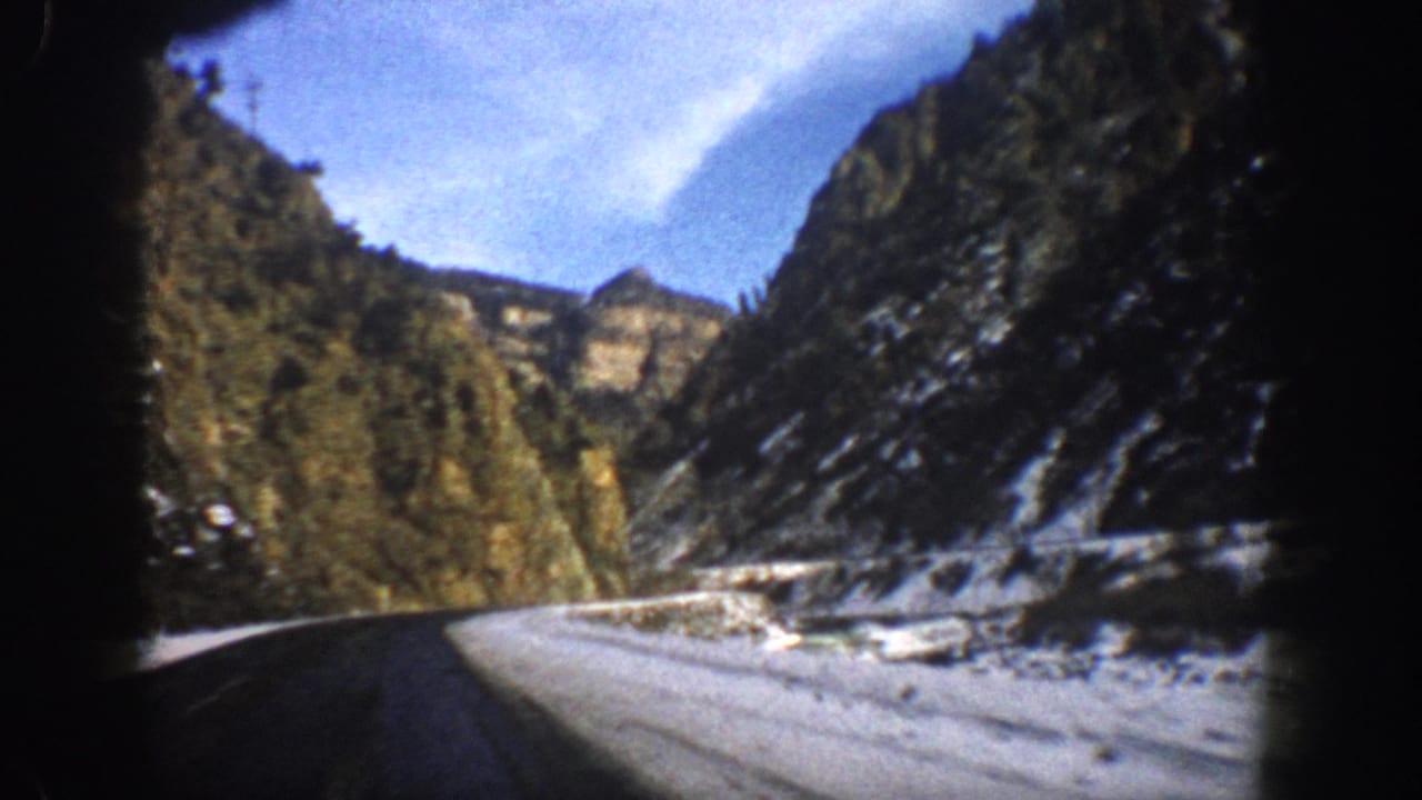 Snow-edged mountain highway bending through a rocky canyon under blue sky.