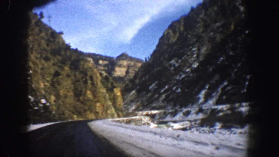 1961 Aspen, Colorado road-view frame with snowy roadside, dark canyon slopes, evergreen trees, and visible 8mm gate shadowing.
