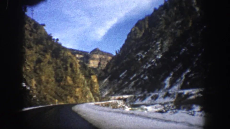 1961 Aspen, Colorado 8mm frame looking along a winter mountain road with snow, trees, cliffs, and soft home-movie blur from motion.