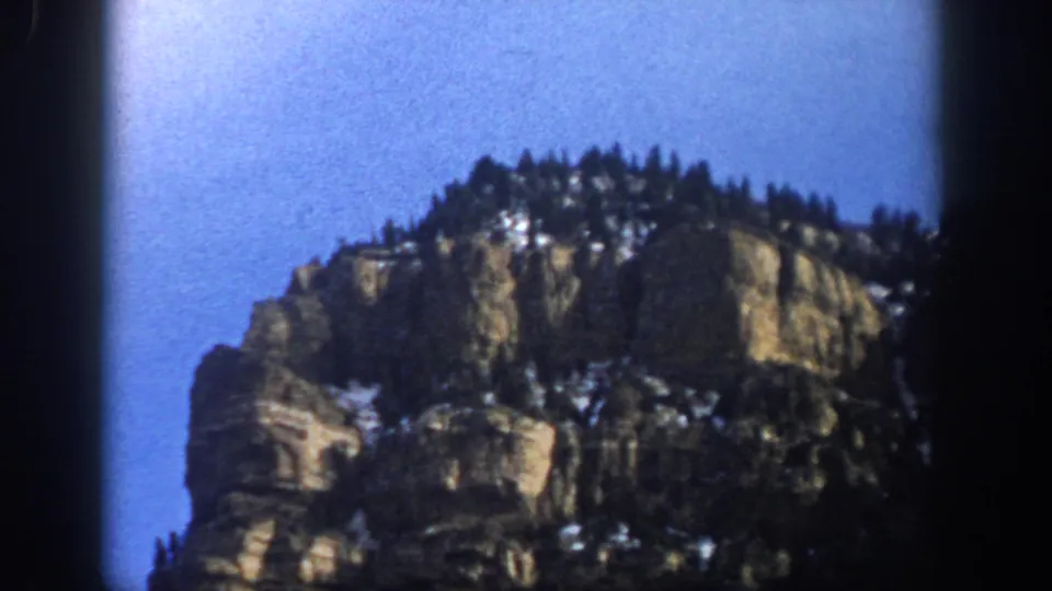 Final 1961 Aspen, Colorado frame showing a rocky mountain face with scattered snow and evergreens, bordered by dark 8mm frame edges.