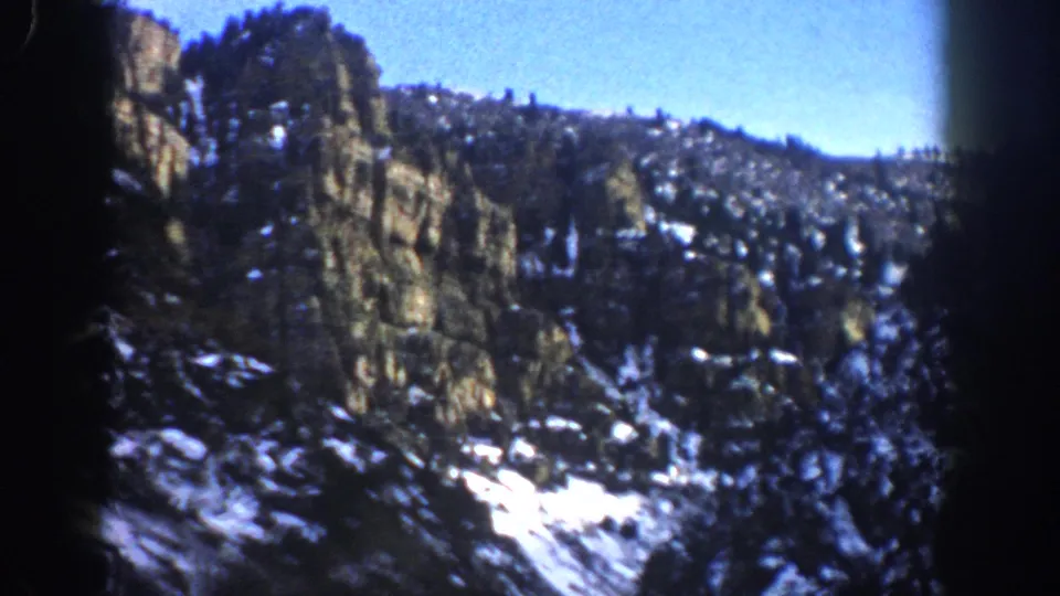1961 Aspen, Colorado home-movie view of a tall rock face, evergreen-covered ridge, snow patches, and clear sky during the pan.