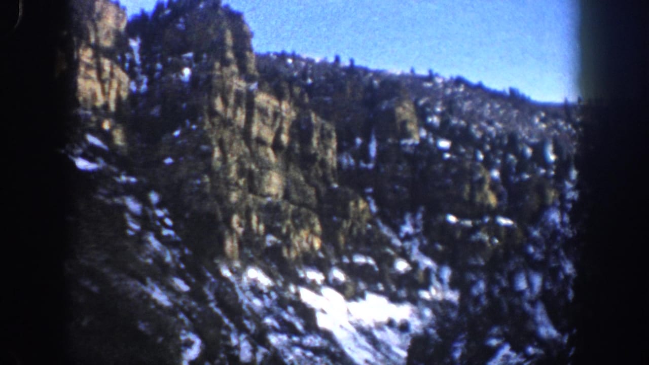 1961 Aspen, Colorado 8mm frame showing a steep rocky cliff, scattered snow, evergreen trees, and dark film borders.