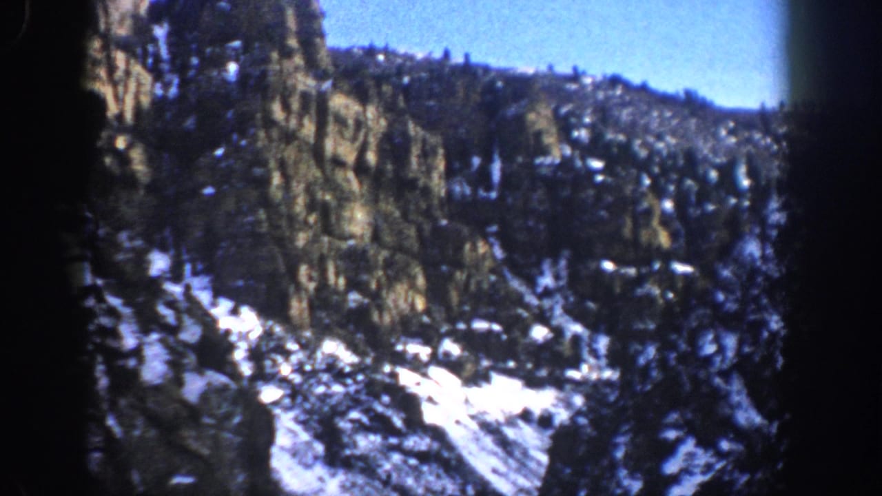 Aspen, Colorado home-movie frame from 1961 showing rugged rock faces, evergreen cover, and remaining snow on a steep mountain slope.