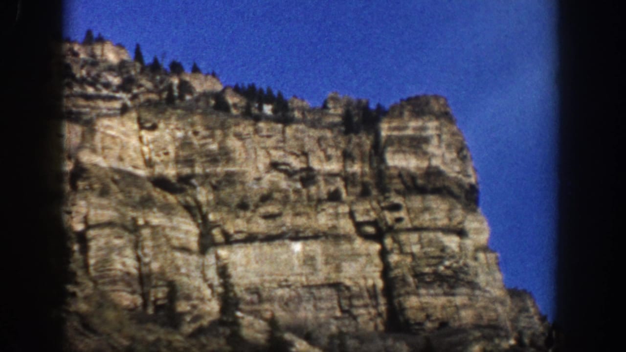 Layered stone cliff with sparse trees along the upper edge.