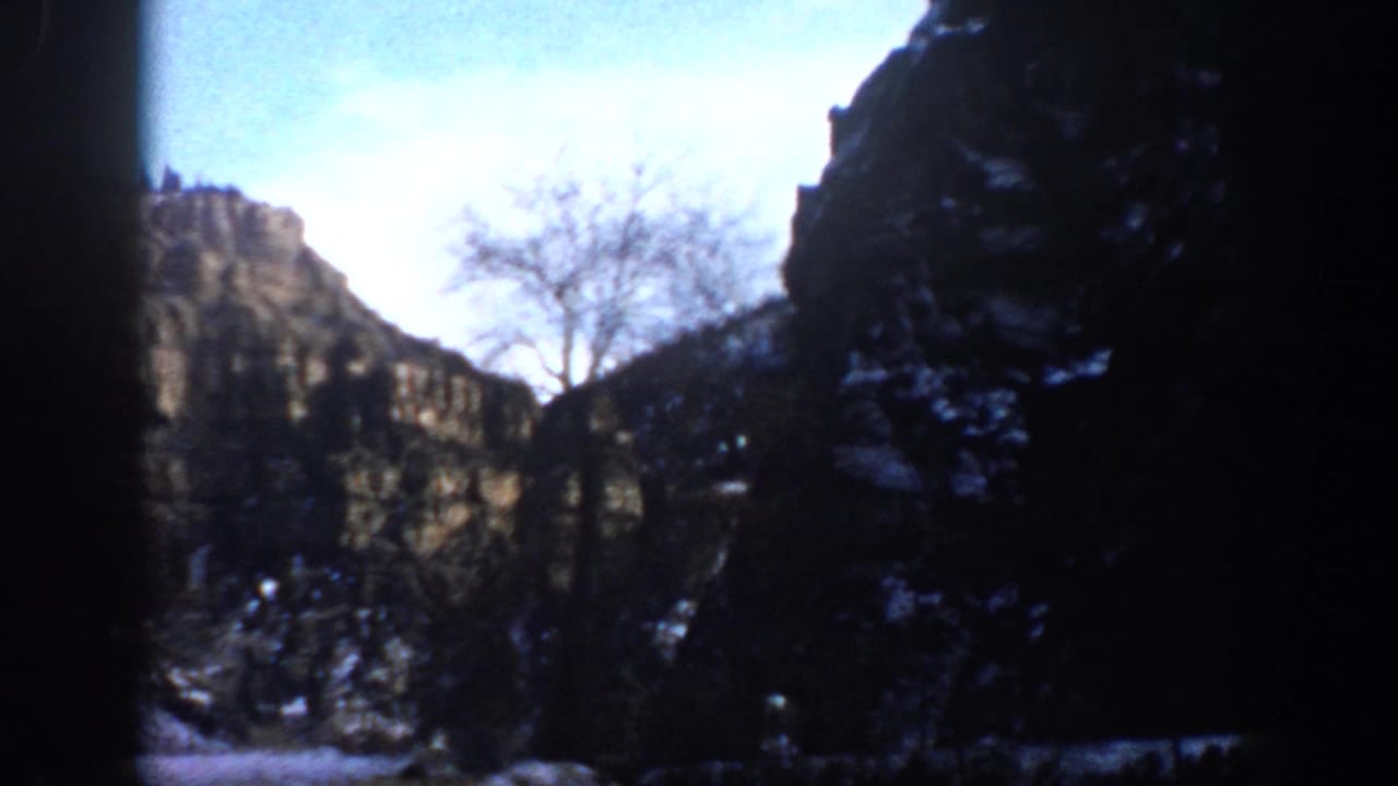 1961 Aspen, Colorado 8mm frame showing rugged canyon rock, sparse snow, bare branches, and dark edge obstruction.