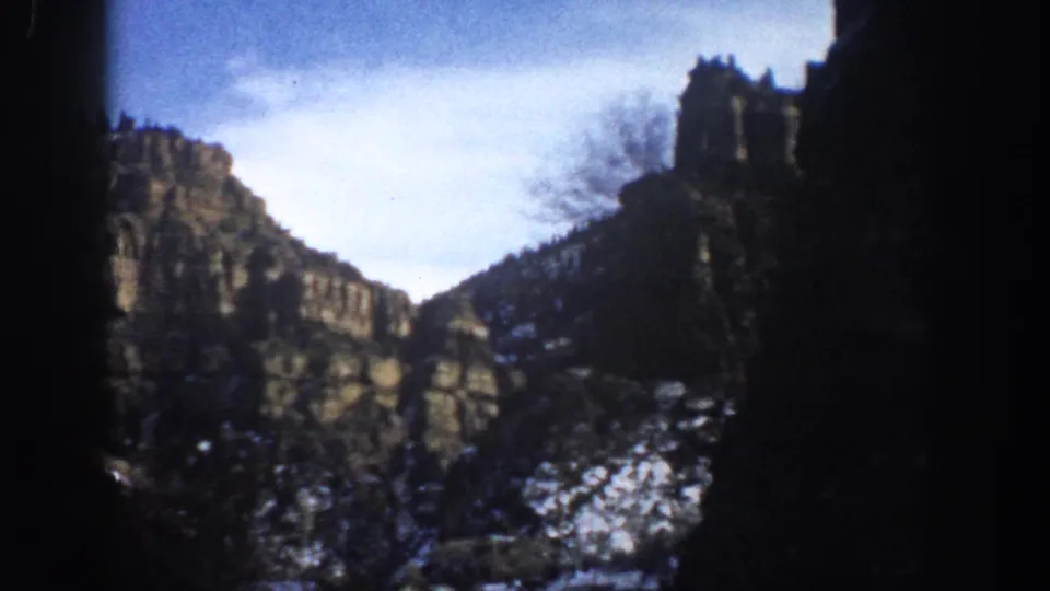 1961 Aspen, Colorado landscape frame showing sunlit rock, snow on slopes, bare branches, and dark edge framing.