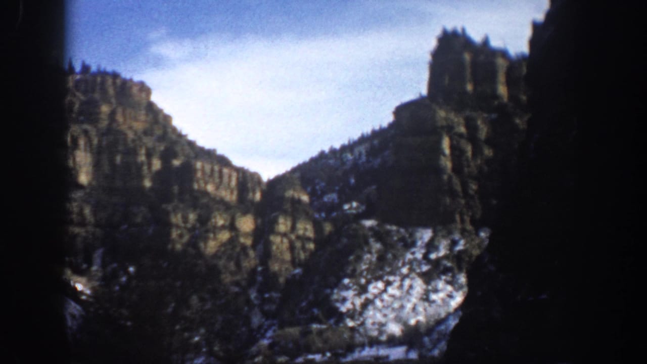 1961 Aspen, Colorado 8mm frame showing rugged canyon formations with snow patches and a blue sky, obscured at the edges by film vignetting.