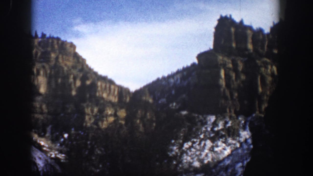 Tall rock formations and snow-speckled slopes viewed across a canyon landscape.