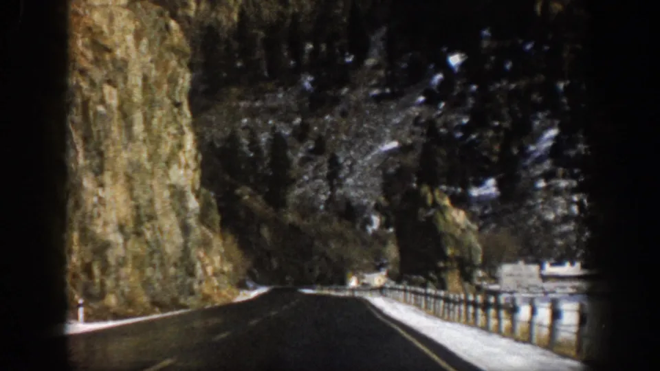 1961 Aspen, Colorado 8mm frame showing a paved mountain road curving through a canyon beside a tall rock wall and roadside railing.