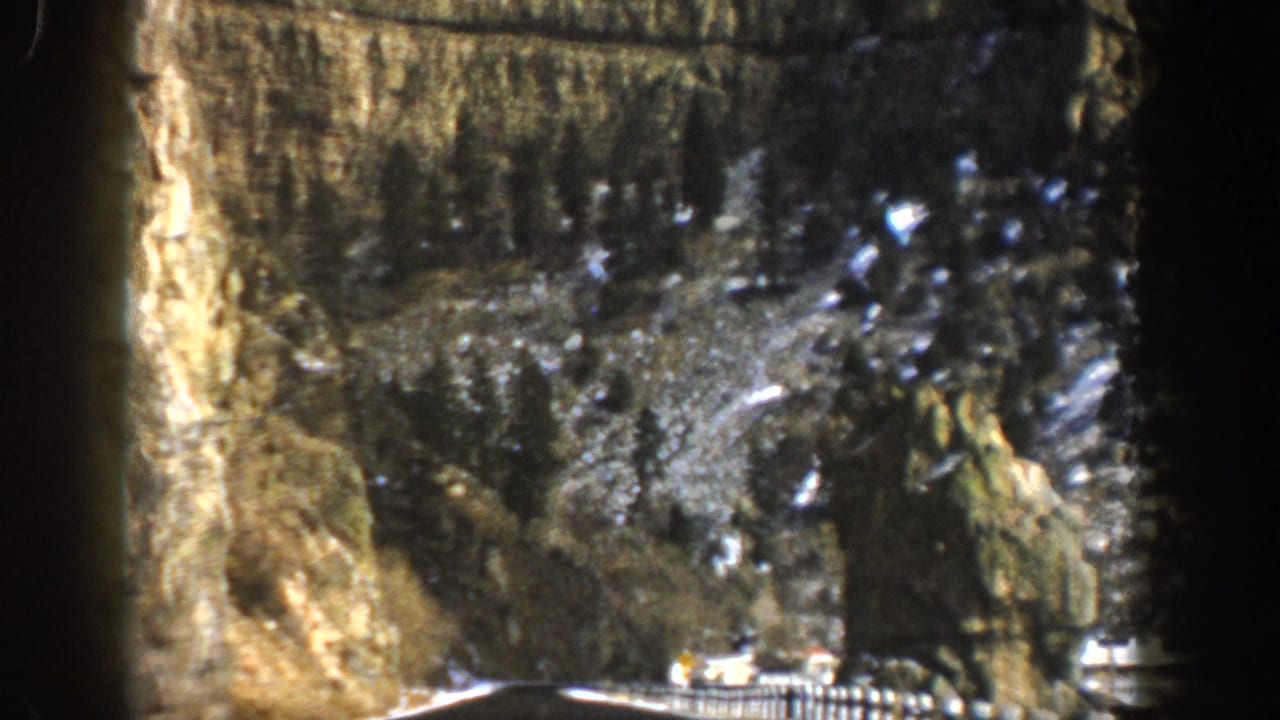 1961 Aspen, Colorado home-movie frame showing a vehicle on a mountain highway beyond a dark tunnel-like edge.