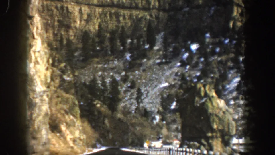 1961 Aspen, Colorado home-movie frame showing a vehicle on a mountain highway beyond a dark tunnel-like edge.