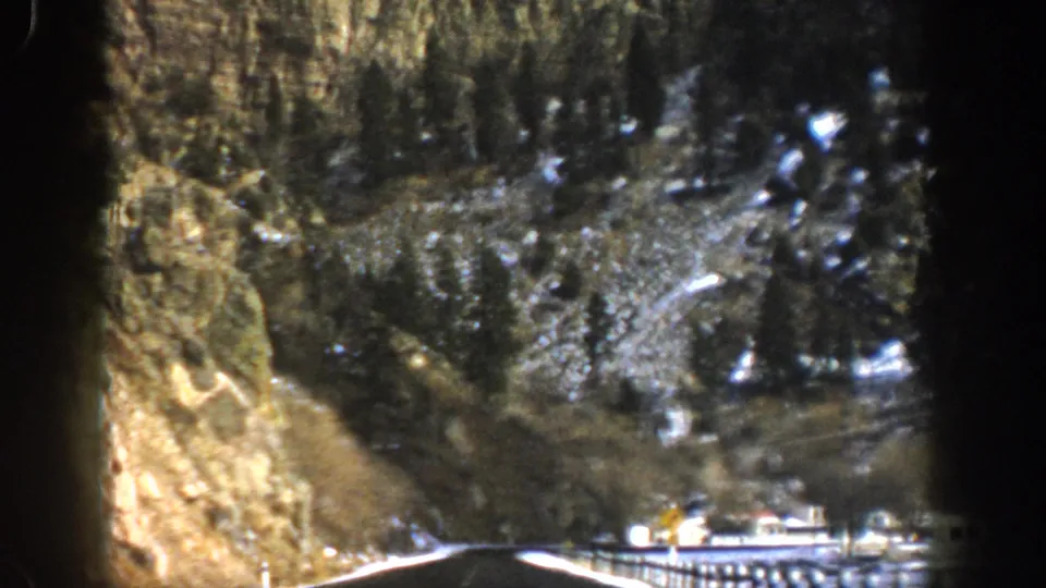 1961 Aspen, Colorado frame looking past a dark film edge toward a snow-dusted mountain road and vehicle.