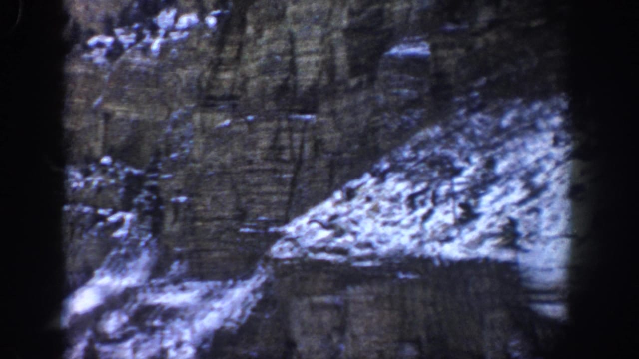 1961 Aspen, Colorado 8mm frame showing a shadowed, snow-dusted rock wall with dark projector edges.