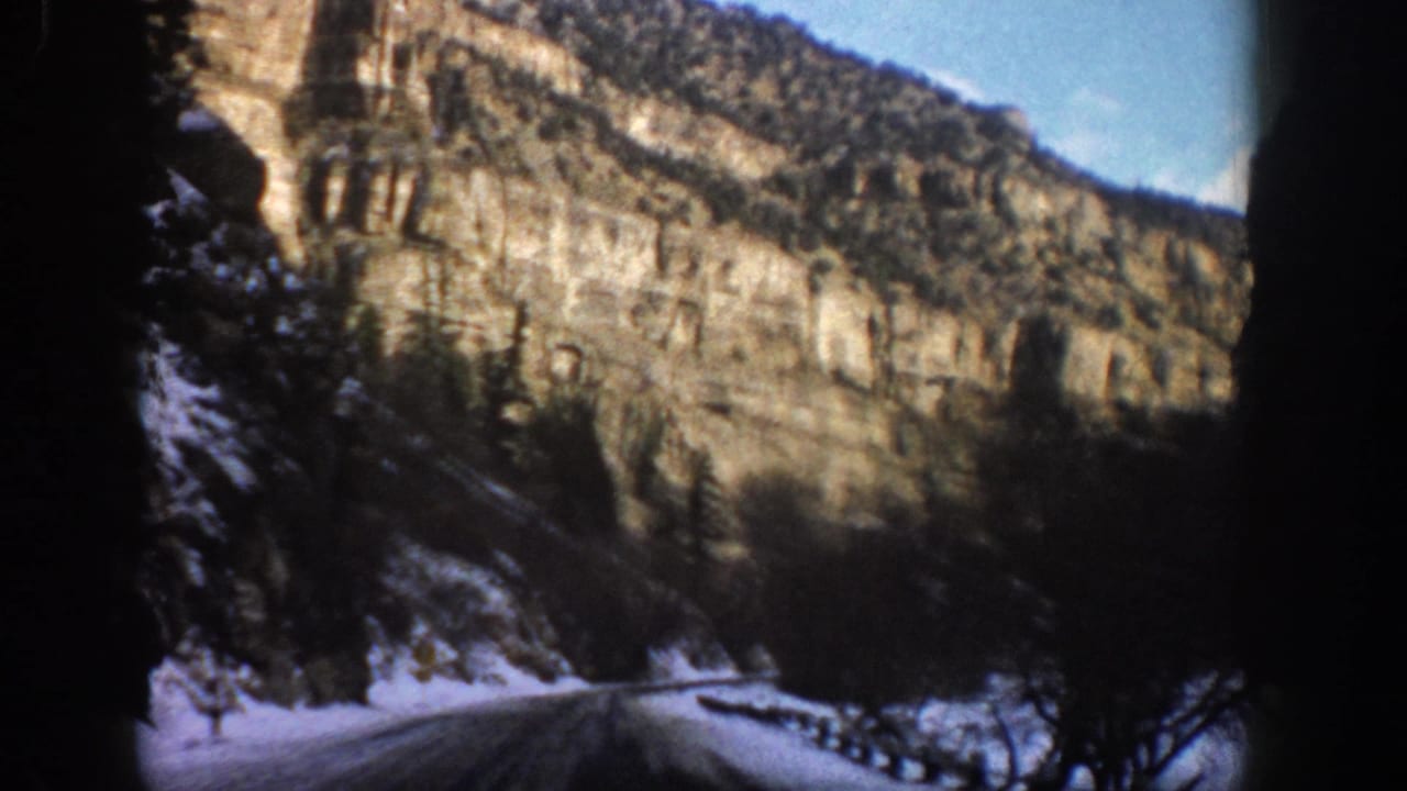 1961 Aspen-area 8mm view of a snow-lined mountain road passing beneath layered cliffs and evergreen trees.