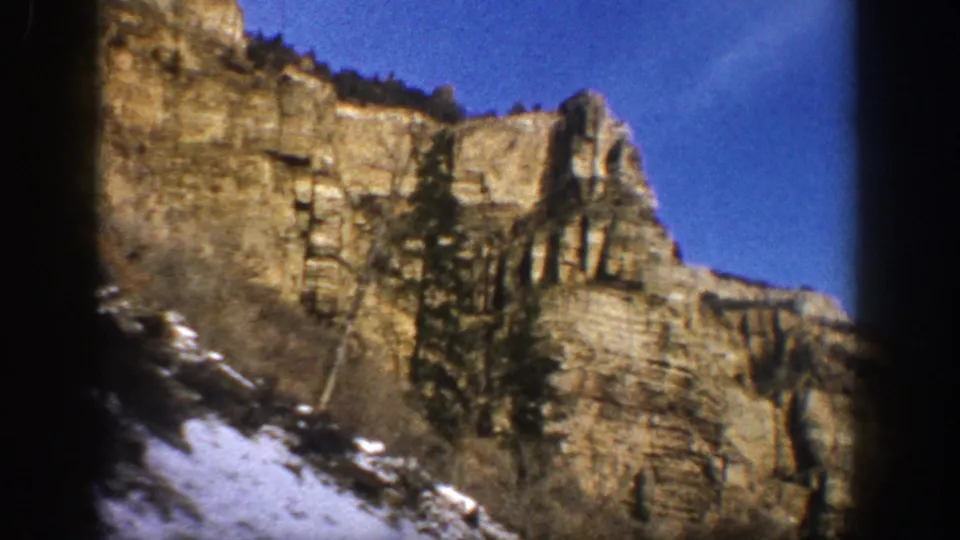 Aspen, Colorado 1961 frame of layered cliffs and conifers beside a snowy mountain road, with visible 8mm softness and blur.