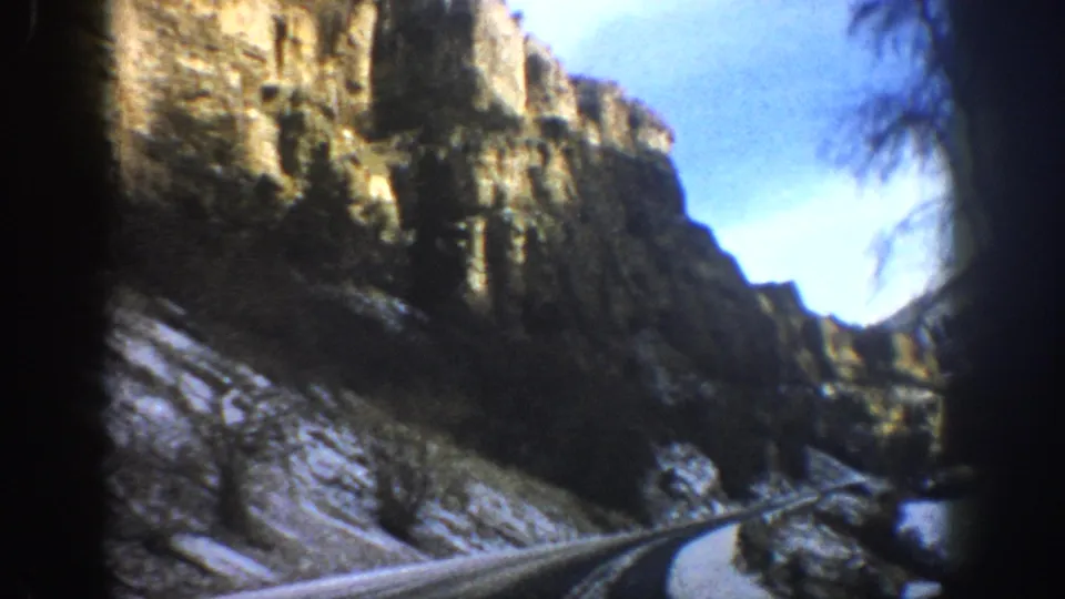1961 Aspen, Colorado frame showing a moving-car view toward a narrow canyon road edged by snow and rock walls.