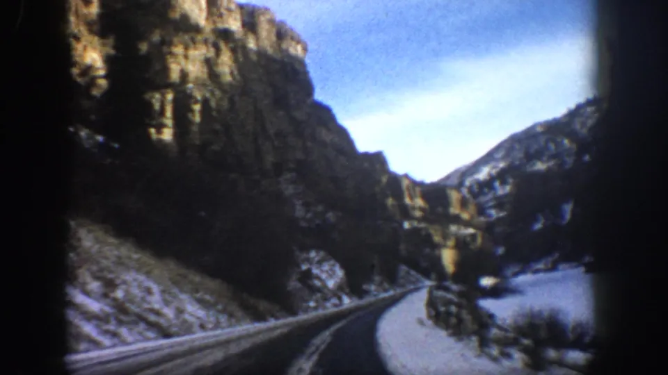 1961 Aspen, Colorado 8mm frame with a winter road winding between high rocky cliffs and snow-covered terrain.