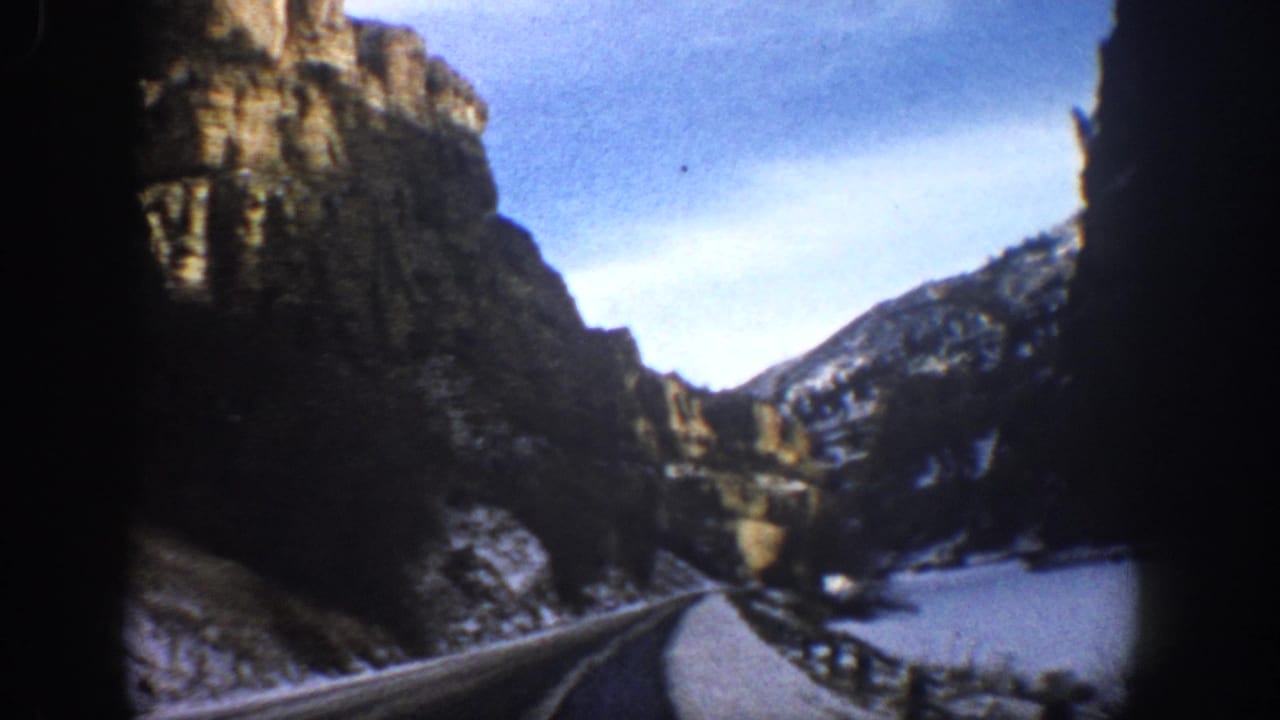 1961 Aspen, Colorado home-movie frame showing a road through snow-dusted canyon cliffs from a moving vehicle.