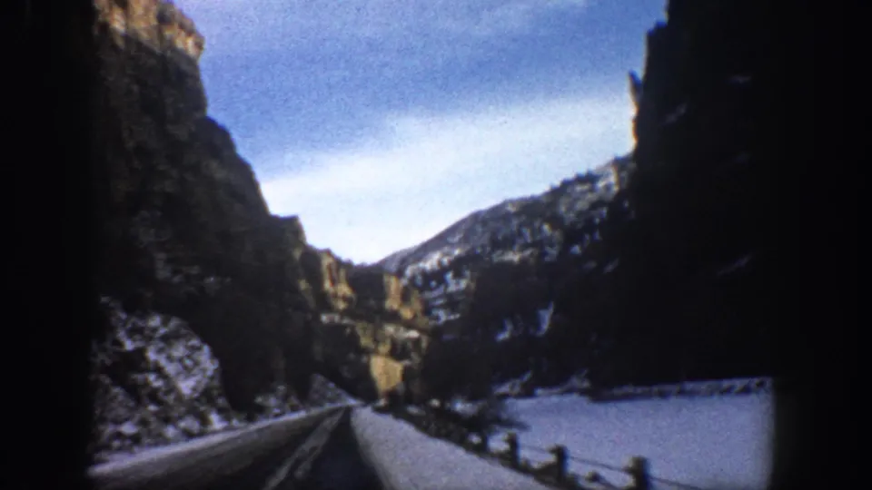Moving-vehicle view of a snowy canyon road near Aspen, Colorado, with rock walls and winter hills visible.
