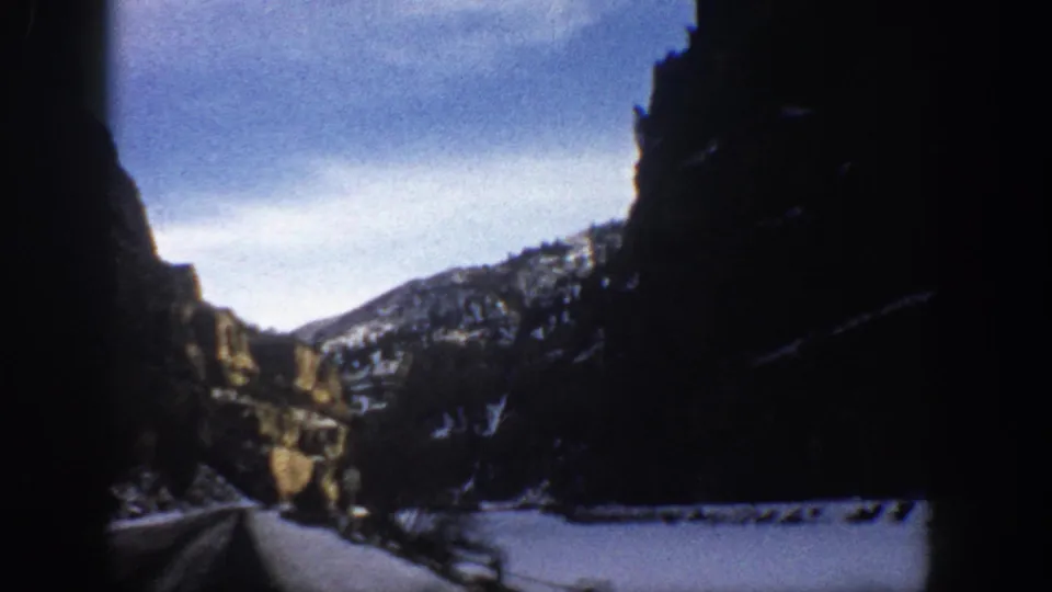 Soft 8mm frame from a 1961 Colorado road trip, showing snow along the roadside and a shadowed canyon wall.