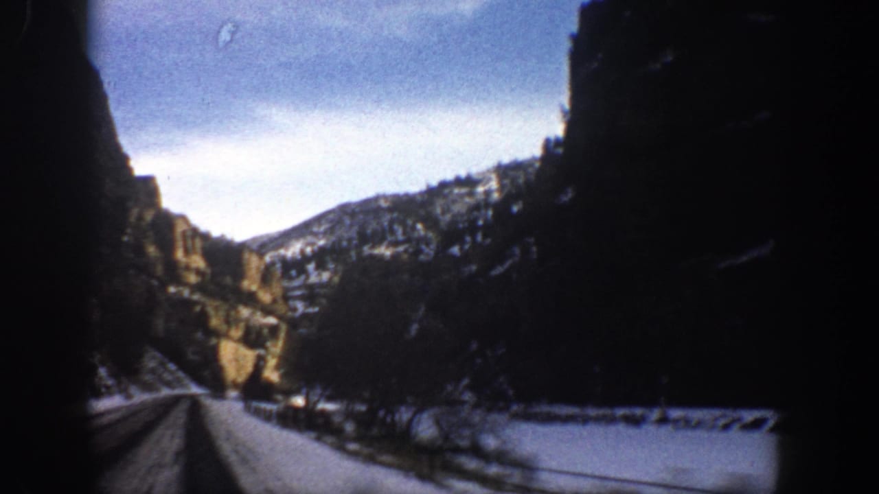 1961 Aspen-area 8mm view from a moving vehicle on a snow-lined mountain road between rugged cliffs.