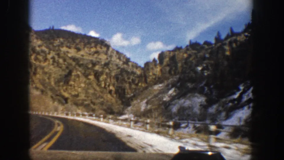 1961 Aspen-area 8mm frame from inside or near a vehicle as the road curves past snow and rocky hillsides.