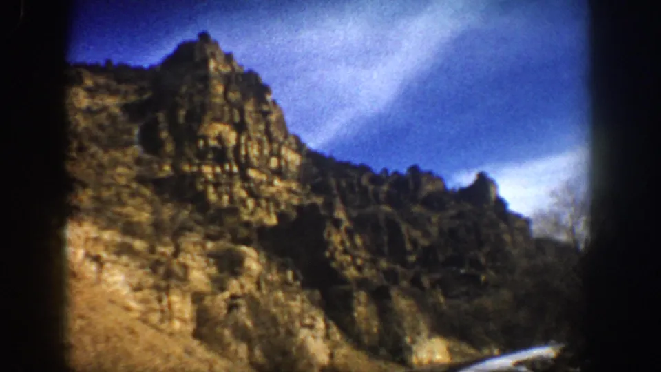 Rugged rock formations and a snowy roadside appear in a 1961 Aspen-area mountain drive frame.