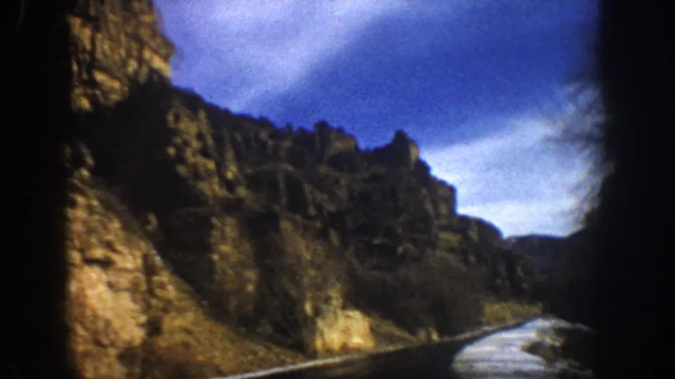 Passenger-view 8mm frame from Aspen-area Colorado showing wet road, roadside snow, and canyon cliffs.