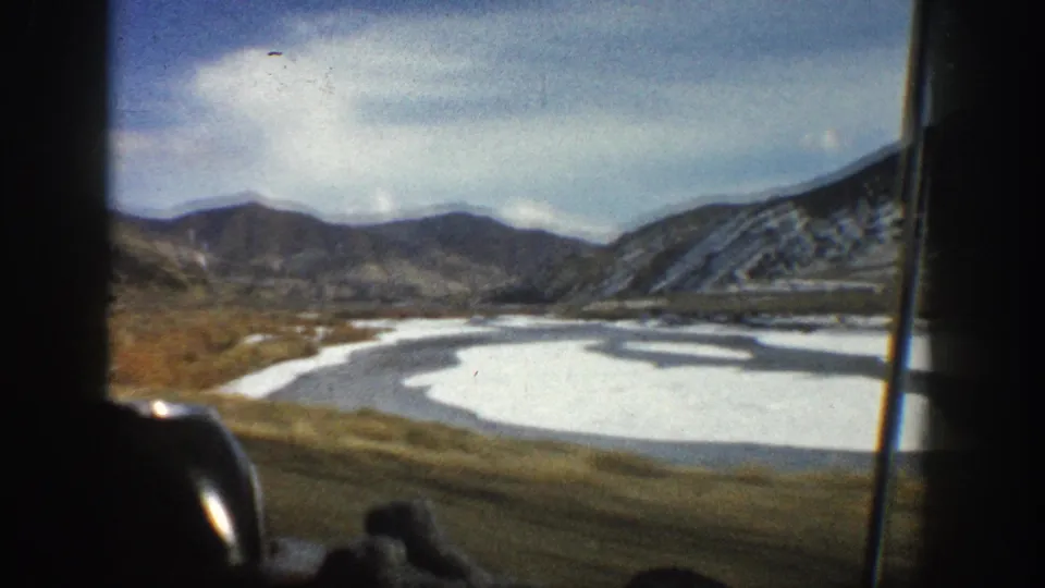 1961 Aspen-area landscape frame showing a frozen river bend, open valley floor, snow-striped hills, and distant mountains.