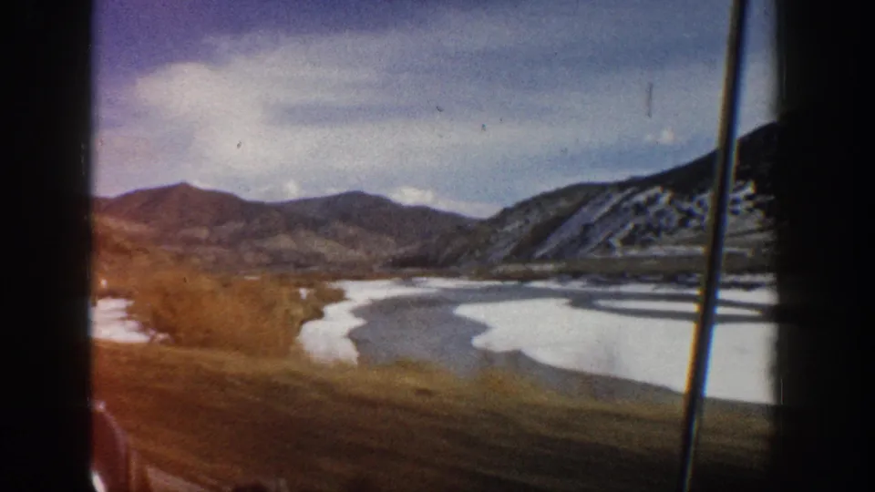 8mm home-movie frame near Aspen, Colorado, looking across a frozen river valley toward layered mountain ridges.