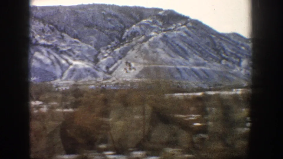1961 Aspen, Colorado 8mm frame with closer snow-streaked hills and a blurred valley foreground from vehicle motion.