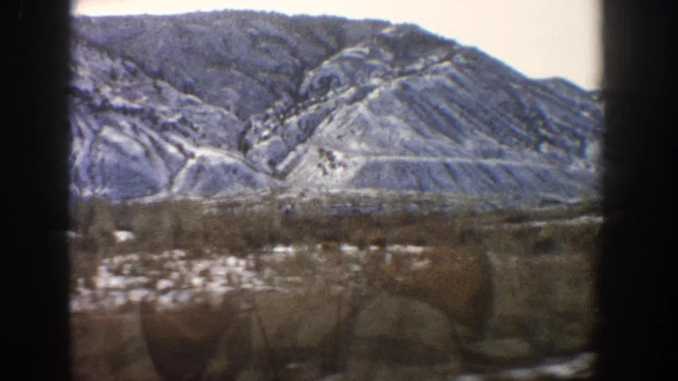 1961 Aspen, Colorado 8mm view of snowy rocky hills, low brush, and open ground through dark vertical borders.