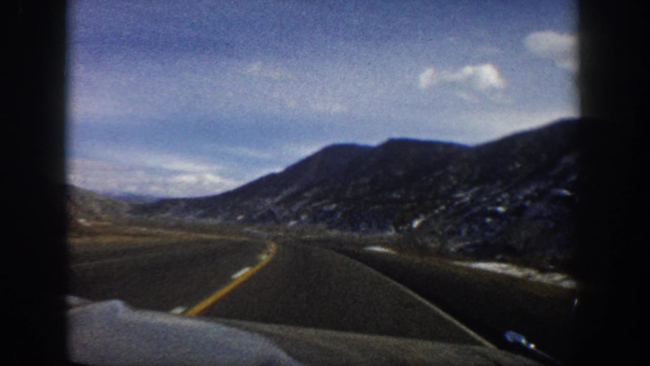 1961 Aspen, Colorado home-movie frame showing a paved road ahead through bare mountain slopes and scattered snow.