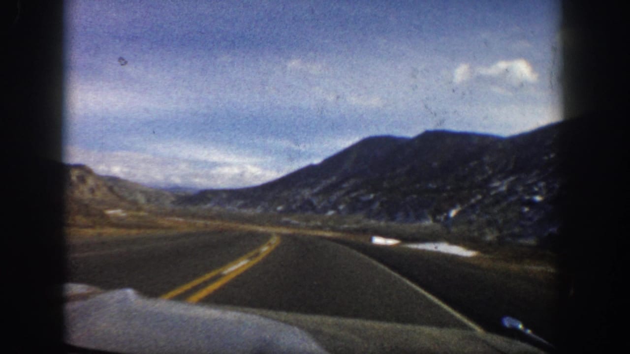 Curving two-lane road through a mountain valley with snow along the roadside.